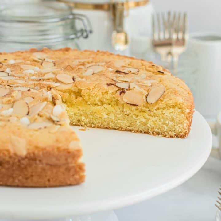 Almond cake on a white cake platter with a slice removed.