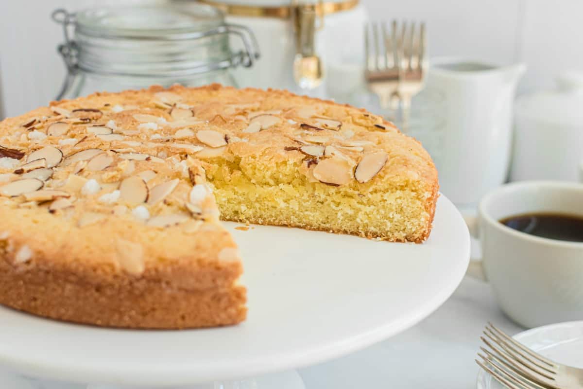 Almond cake on a white cake platter with a slice removed.