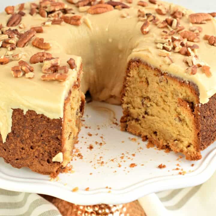 Brown sugar pound cake with caramel glaze on a white cake plate with a big chunk removed.