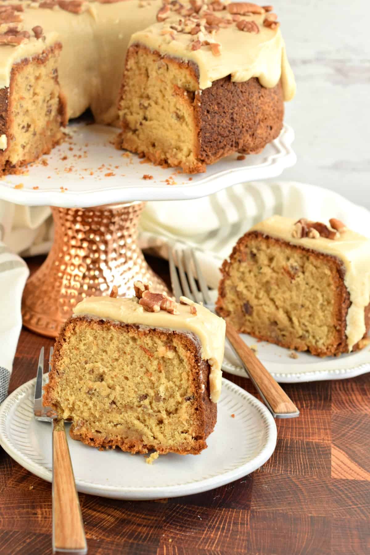 Two slices of pound cake served on white plates with a fork. Whole cake in background on a cake platter.