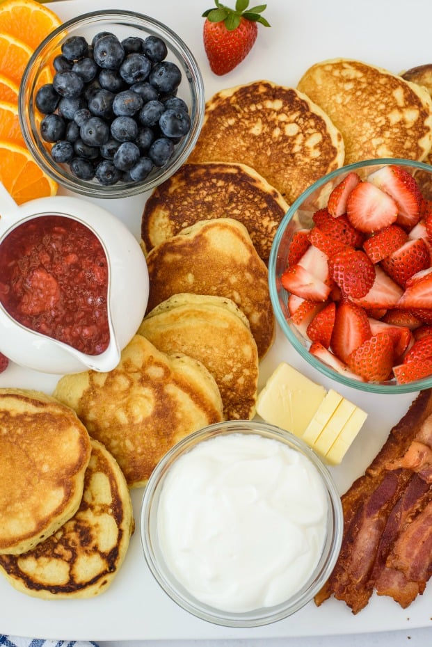 Pancake board with fresh berries, whipped cream, bacon, and berry syrup.