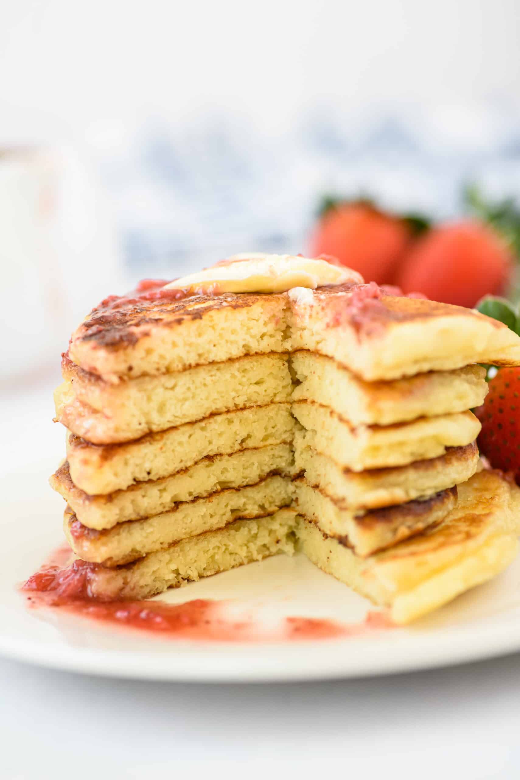 Stack of 6 pancakes with big slice taken out. Topped with berry syrup.