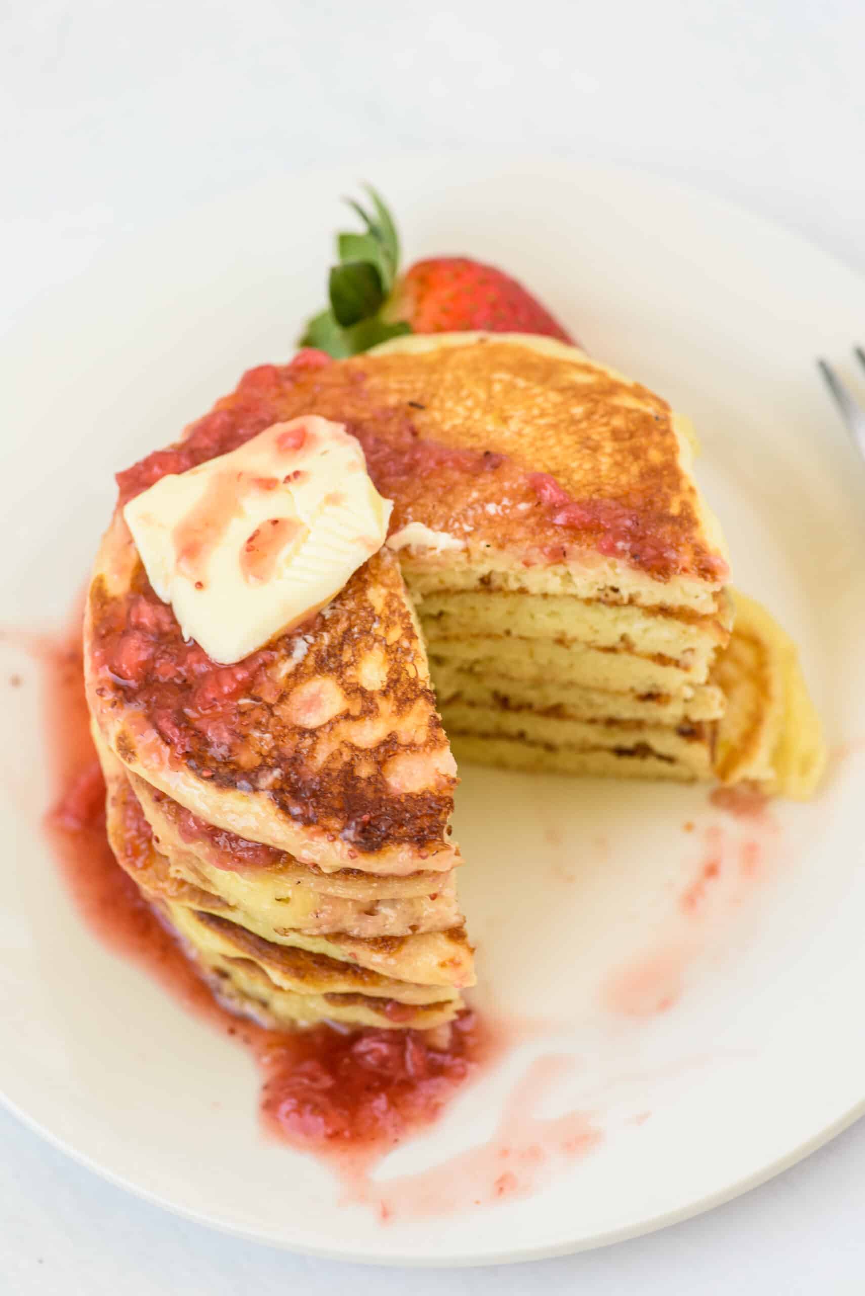 Buttermilk pancakes on a white plate with butter and berry syrup.