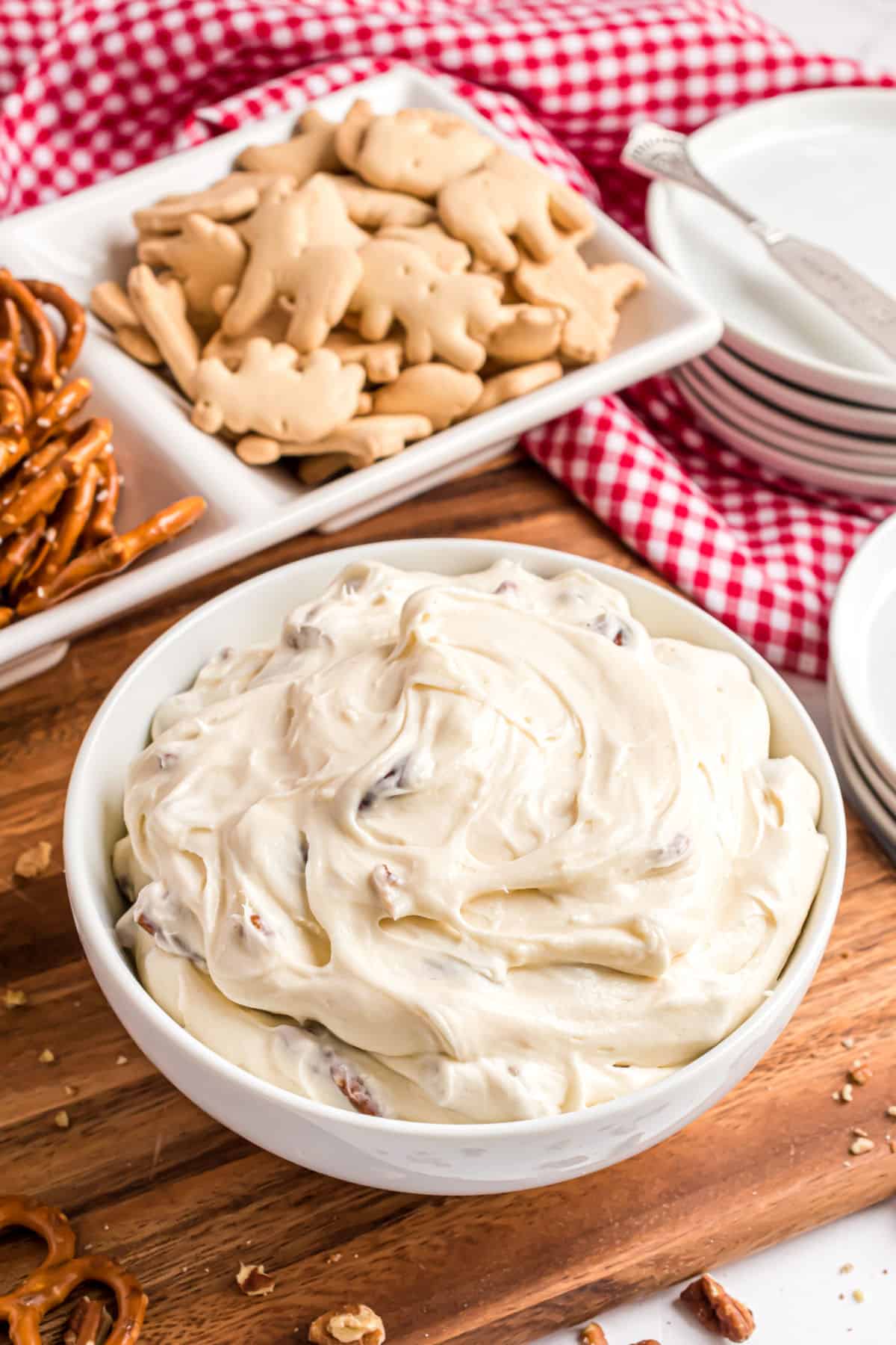 Cheesecake dip in a white bowl served with animal crackers and pretzels.