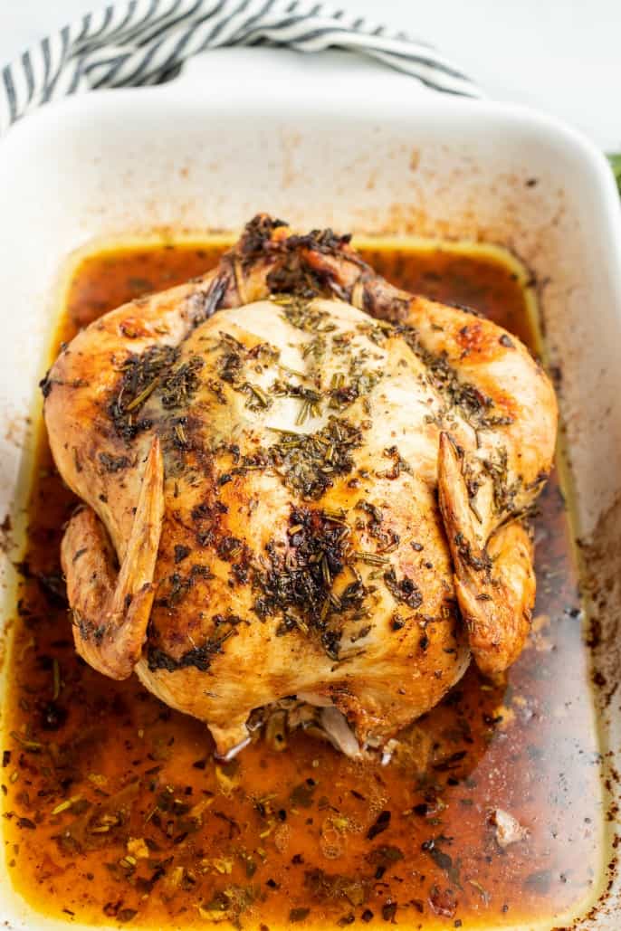 Whole roasted chicken in white roasting pan with all the juices.