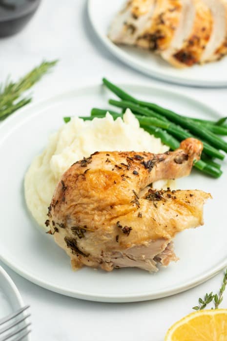 Leg and thigh of chicken on plate with mashed potatoes and green beans.