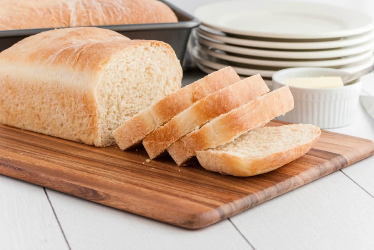 Sliced loaf of white bread on a dark wooden cutting board.