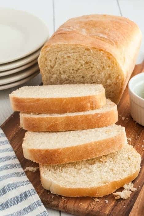 One loaf of homemade white bread on a wooden cutting board, cut into slices.