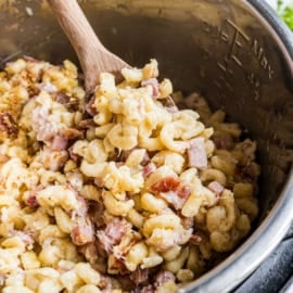 Creamy macaroni with diced ham and bacon, reminiscent of instant pot chicken cordon bleu, being stirred in a metal pot with a wooden spoon.