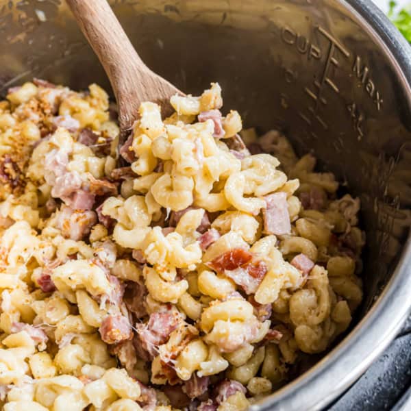 Creamy macaroni with diced ham and bacon, reminiscent of instant pot chicken cordon bleu, being stirred in a metal pot with a wooden spoon.