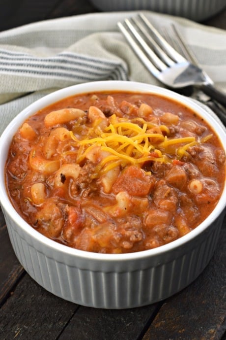 Gray ramekin with american goulash topped with shredded cheddar cheese.