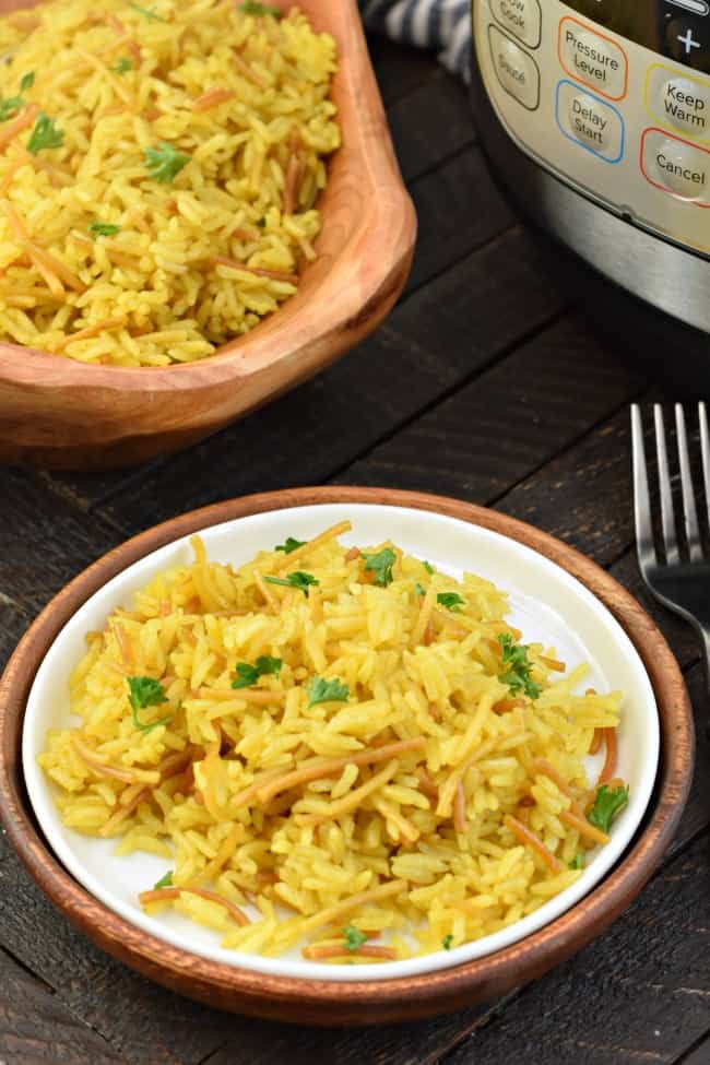 White plate with a serving of rice a roni. Wooden bowl in background as well as Instant Pot.