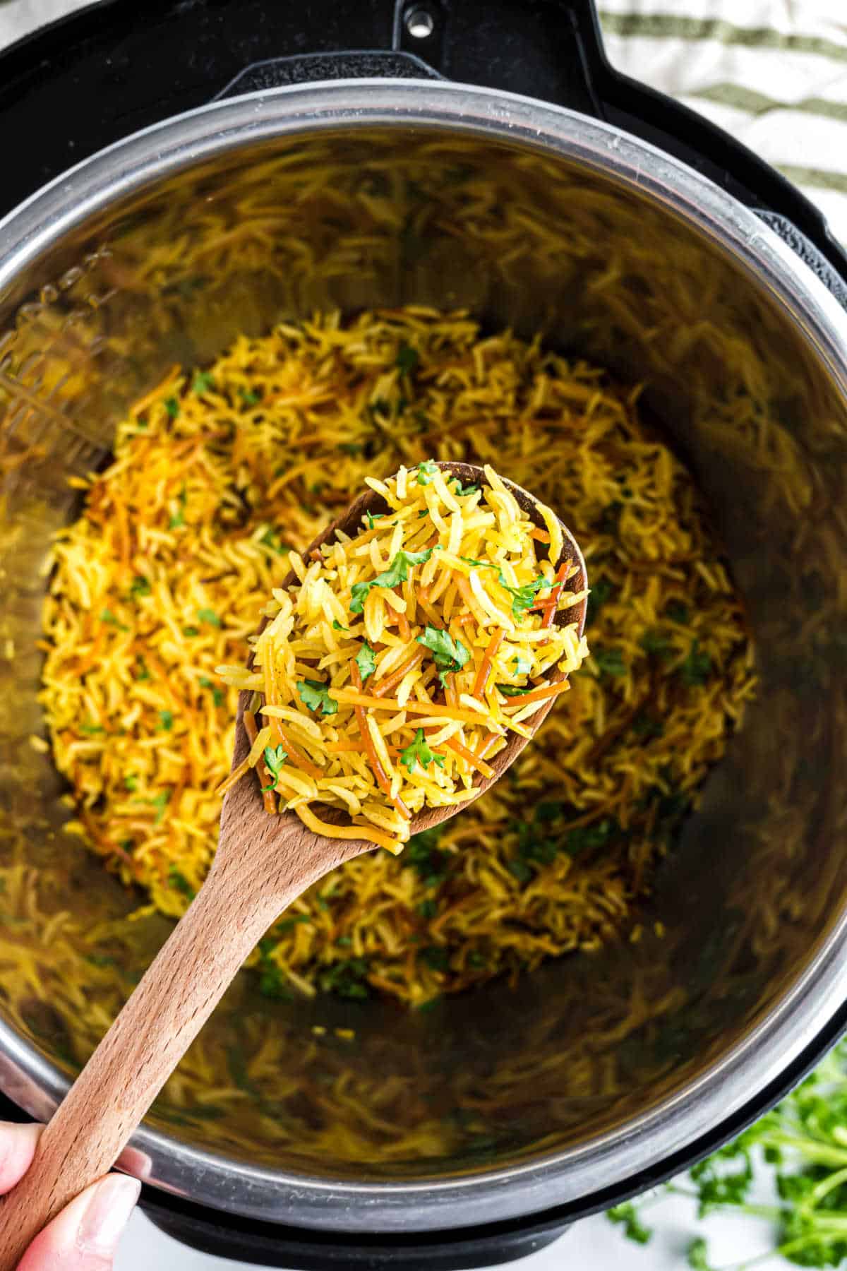 A wooden spoon holds yellow rice with herbs above a pot filled with more instant pot Rice-A-Roni.