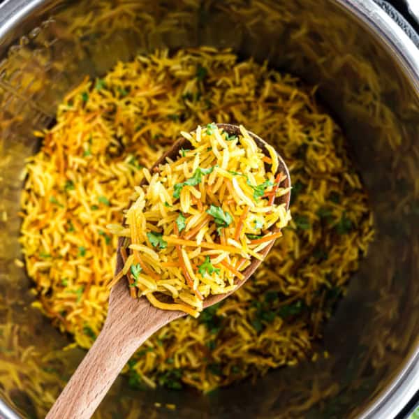 A wooden spoon holding yellow seasoned instant pot Rice-A-Roni with herbs over a pot of the same rice.