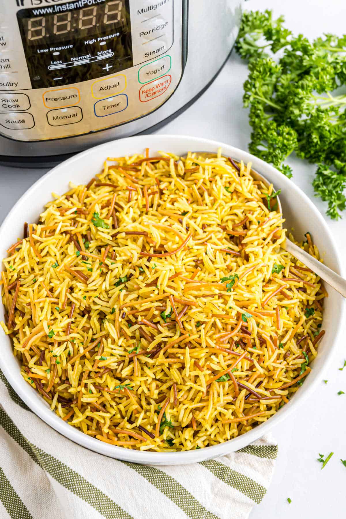 A bowl of cooked yellow rice with vermicelli, just like Instant Pot Rice-A-Roni, sits next to parsley and an Instant Pot.