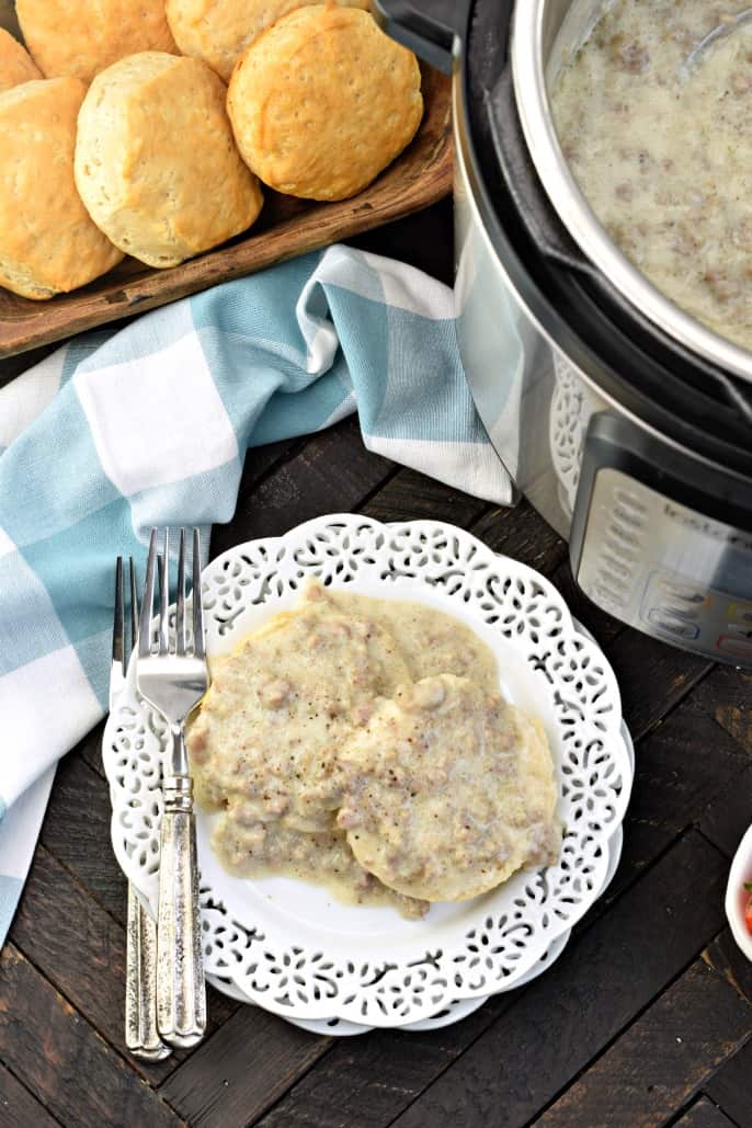 White plate with biscuits and gravy. Instant Pot filled with more sausage gravy, and fresh baked biscuits in a wooden bowl.