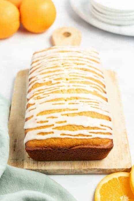 Loaf of orange bread on a wooden cutting board drizzled with orange glaze. 