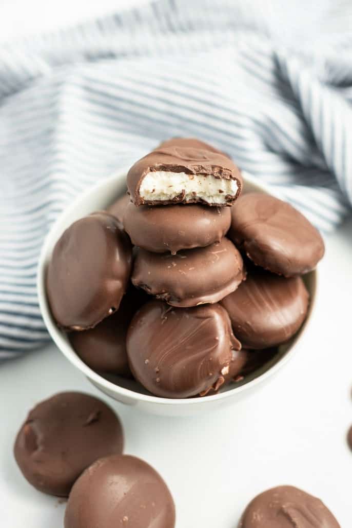 White bowl filled with homemade Peppermint Patties. One broken in half on top of pile so you can see filling.