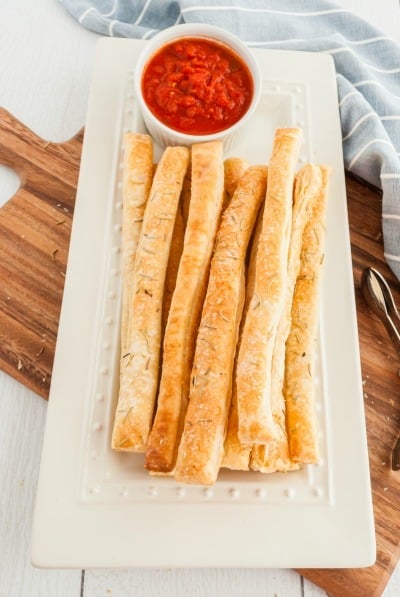 Puff Pastry bread sticks on a white rectangular plate served with marinara sauce.