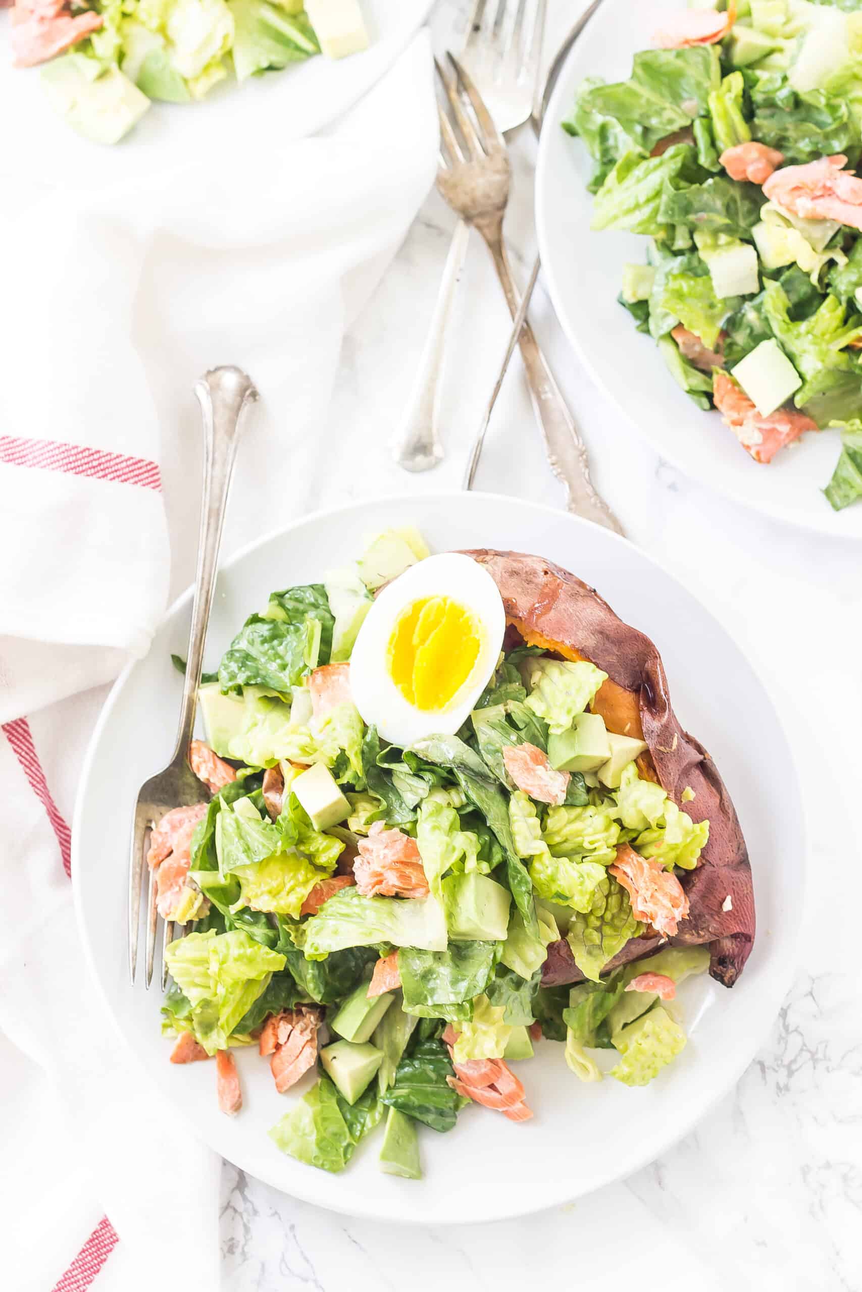 White dinner plate with baked sweet potato topped with caesar salad.