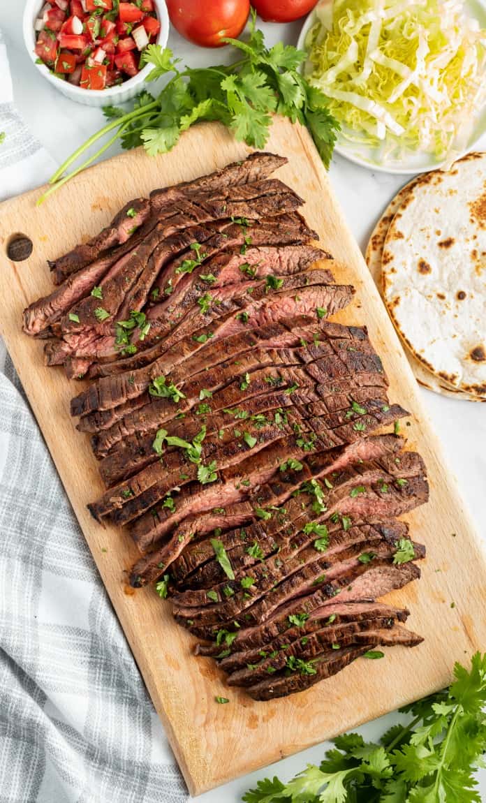 Grilled flank steak sliced thin on a wooden cutting board and sprinkled with chopped cilantro.