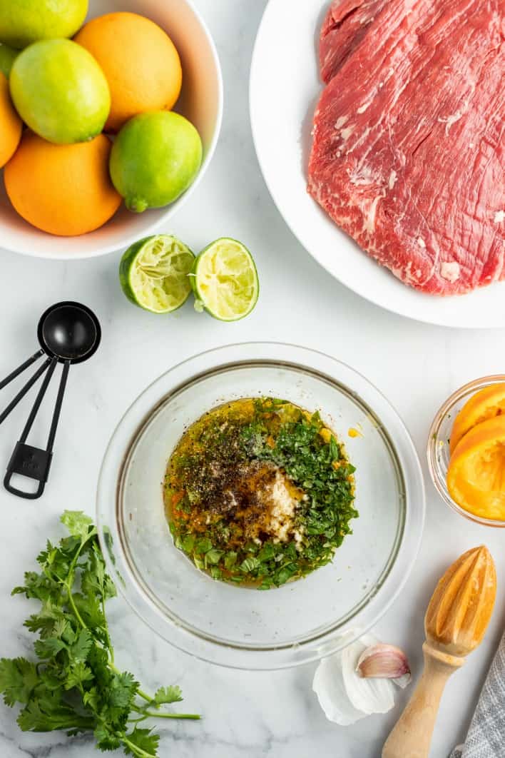 Ingredients needed for carne asada, including flank steak, limes, oranges, and cilantro.