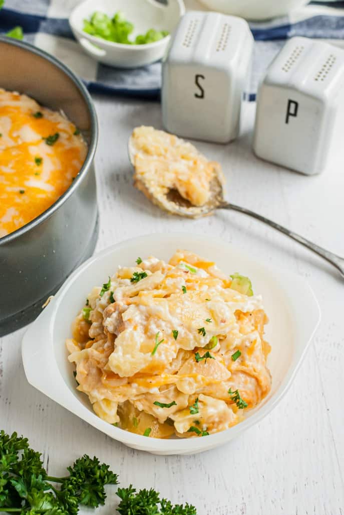 Scoop of au gratin potatoes in a white dish with spoon on side.