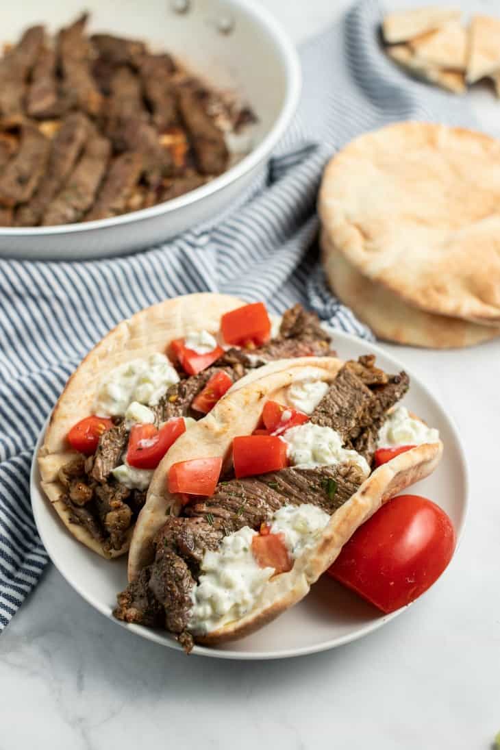 Two pitas stuffed with sliced beef and topped with tzatziki sauce and diced tomatoes.