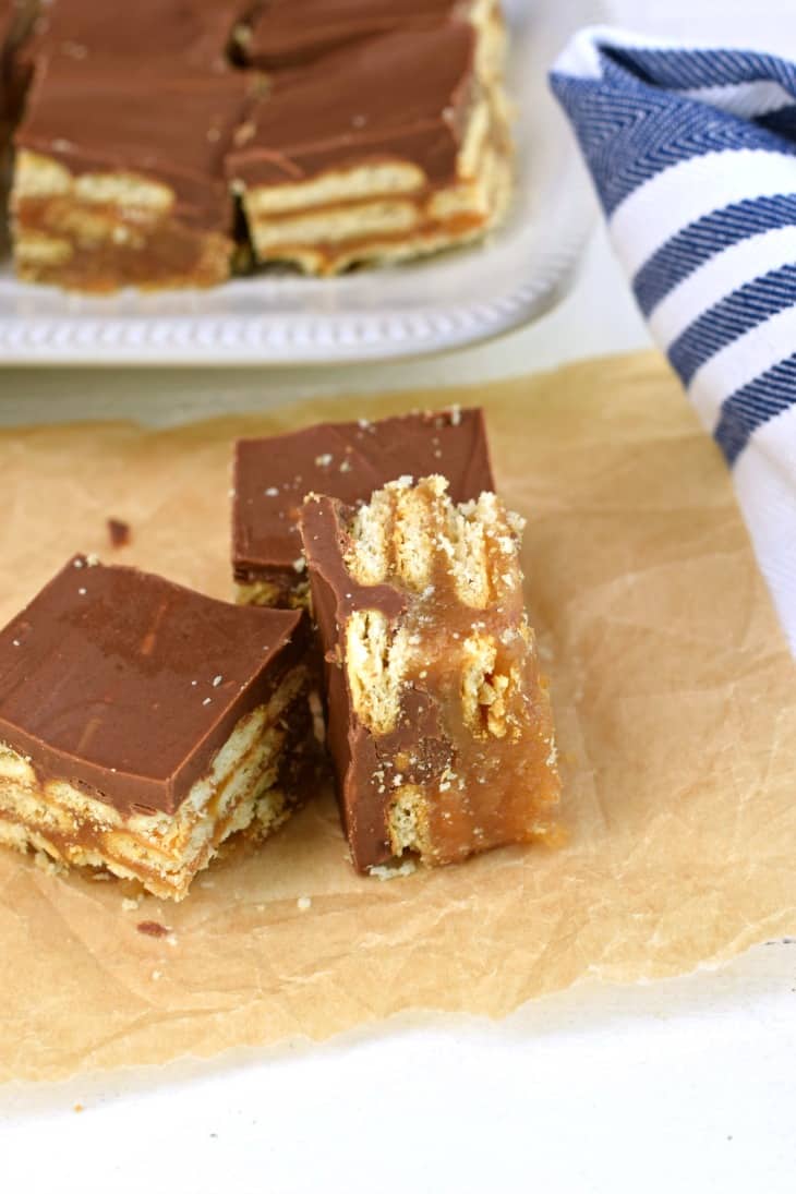 Piece of parchment paper topped with 3 pieces of cracker bars, one turned on it's side and oozing with caramel.