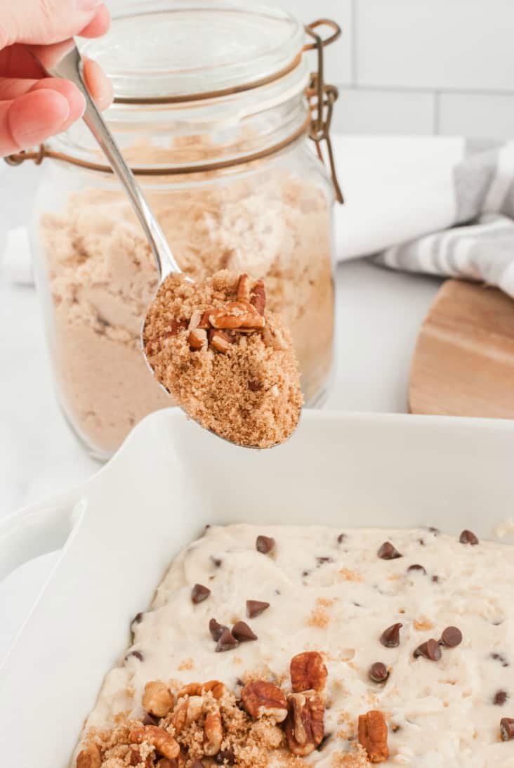 Brown sugar crumb topping being sprinkled on unbaked chocolate chip cake.