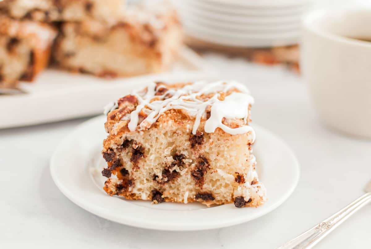 Slice of chocolate chip coffee cake with vanilla glaze on a white plate.