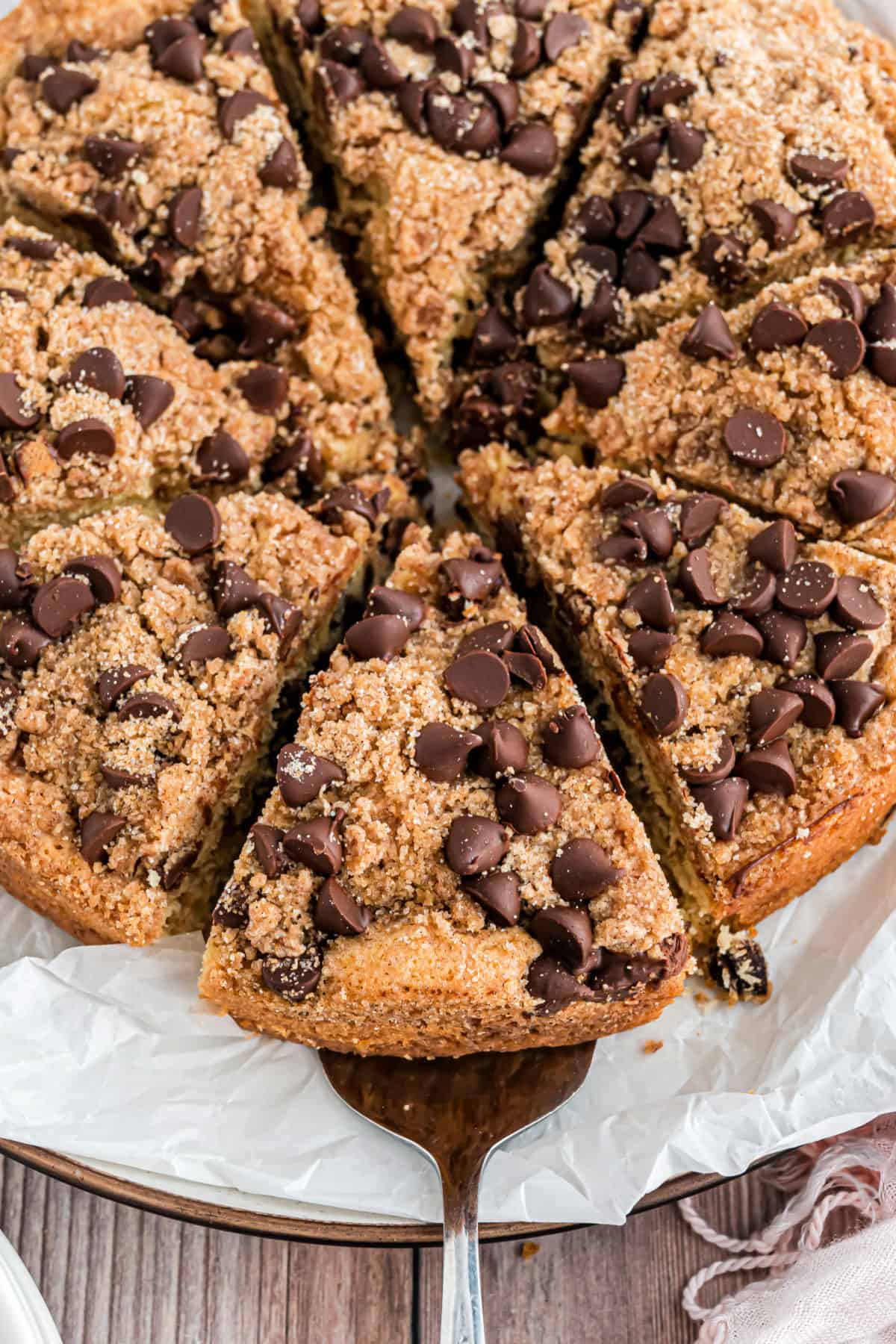 Chocolate chip coffee cake sliced with a piece being removed.