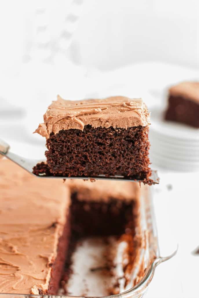 Slice of chocolate cake with chocolate frosting on a spatula being lifted out of the cake pan.