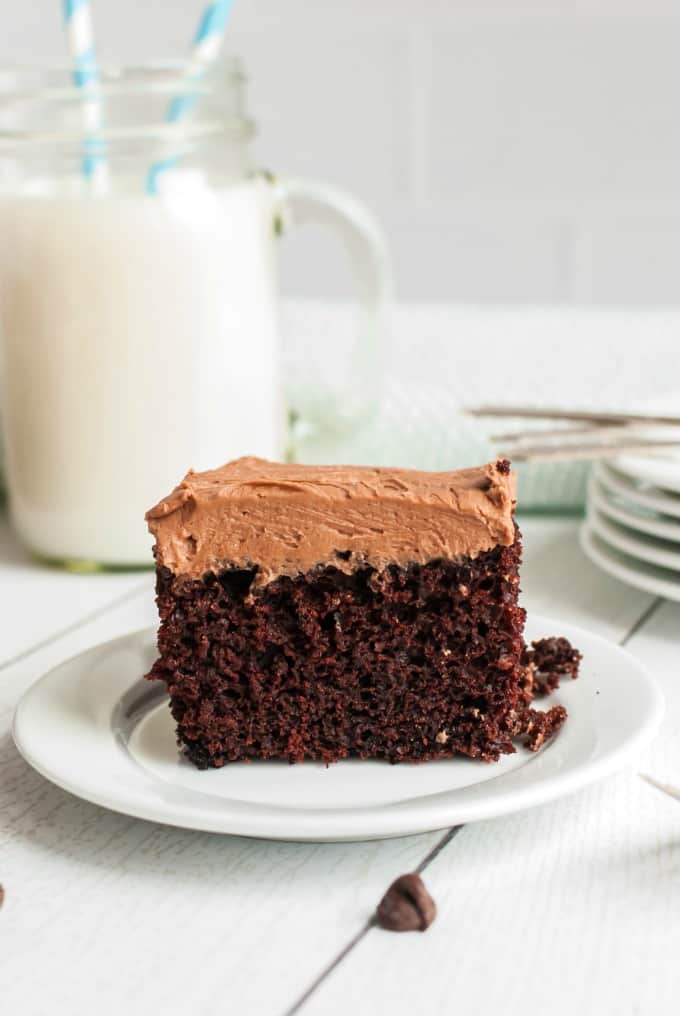 Chocolate frosted wacky cake on a white plate with a mug of milk.