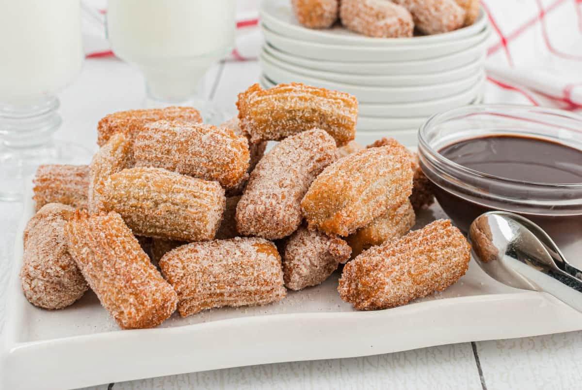 Plate of churro bites with dark chocolate dipping sauce on the side.