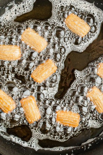 Churro Bites in a hot cast iron skillet in oil frying.