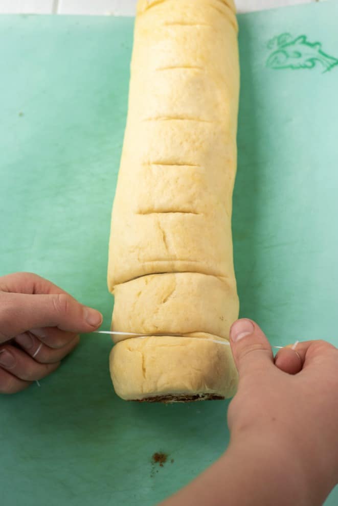 Roll of cinnamon rolls being cut with a twine.
