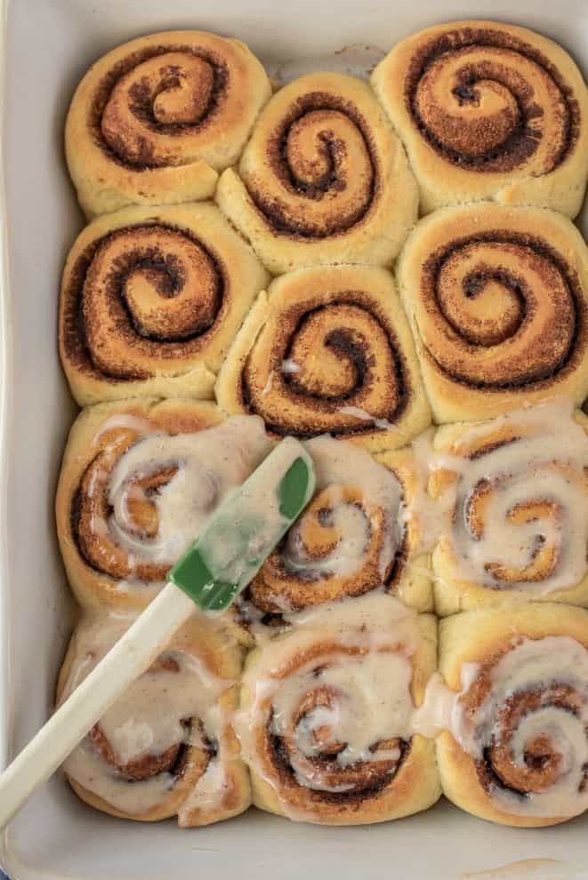 Baking cinnamon rolls being frosted with cream cheese icing.