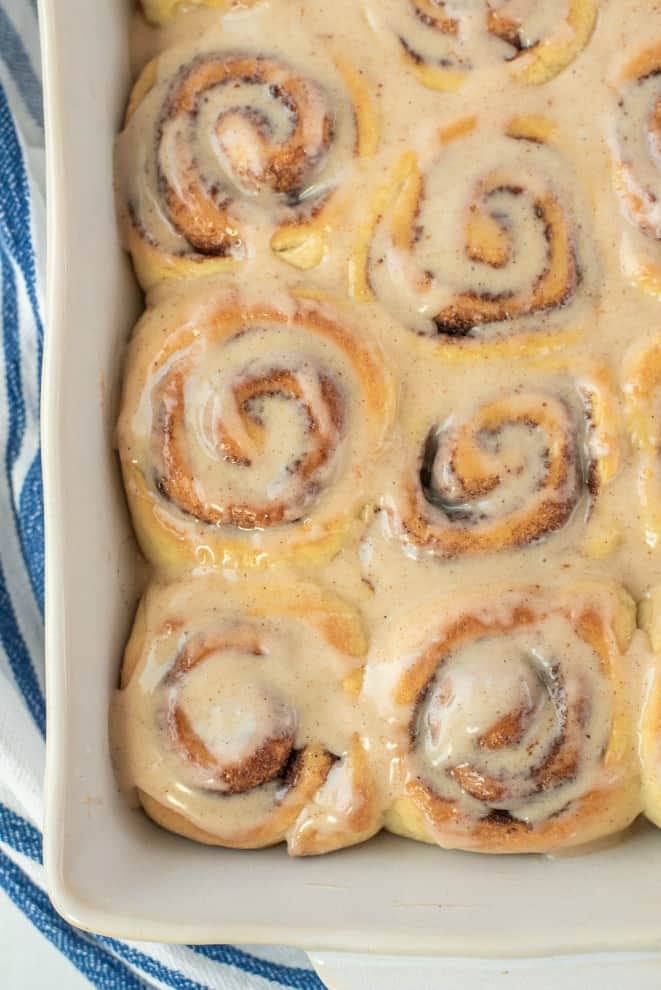 Pan with baked cinnamon rolls covered in melted icing.