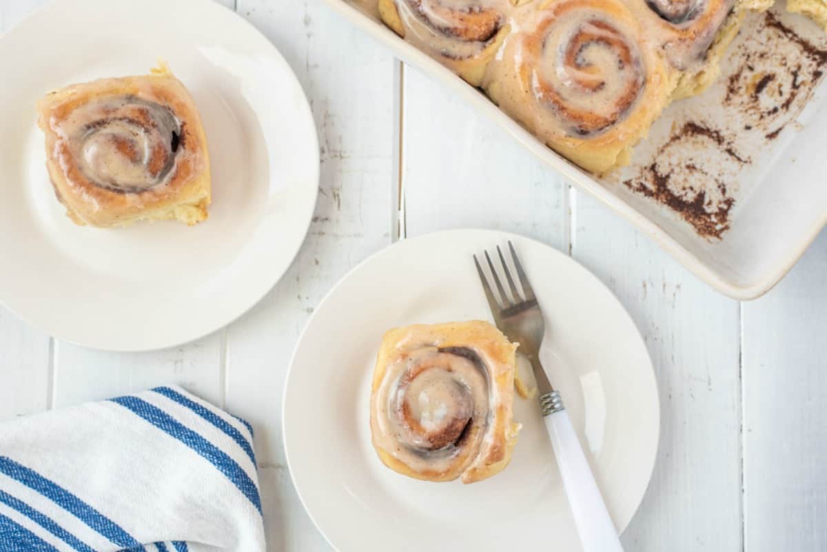 Pan of cinnamon rolls with two rolls on white plates.