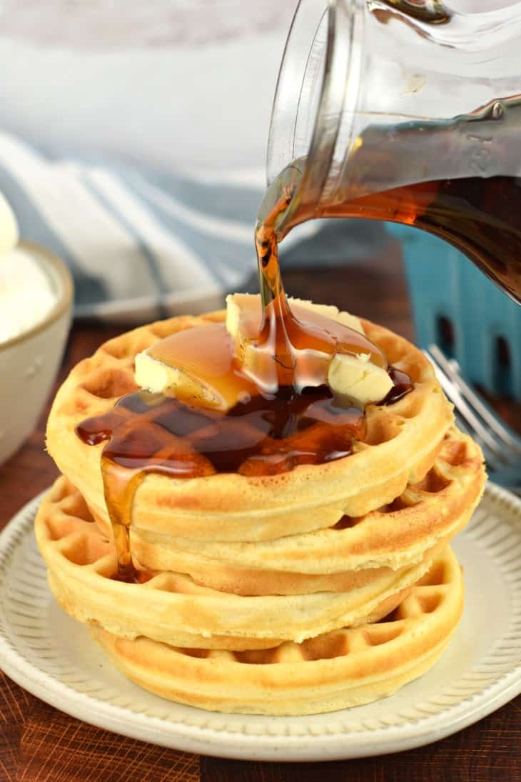 Stack of four waffles with maple syrup being poured over the top.