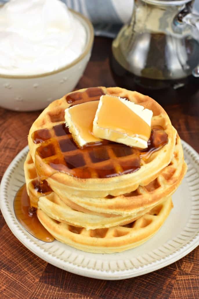 Stack of 4 waffles, two pats of butter and maple syrup drizzled on top.