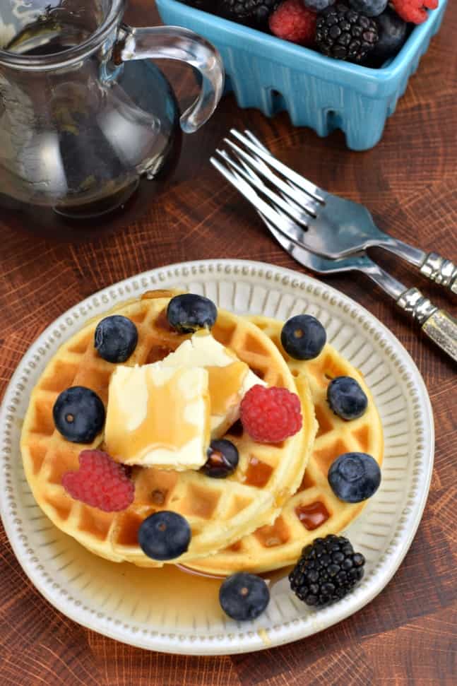 Two homemade waffles topped with butter, syrup, and fresh blueberries, raspberries, and blackberries.