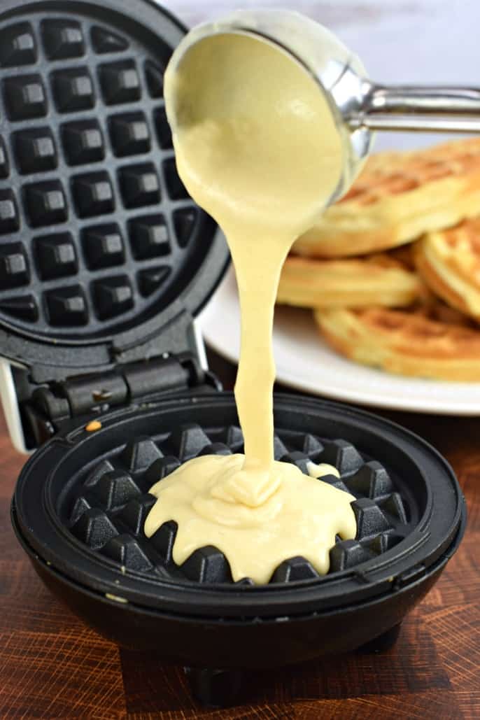 Metal scoop pouring batter onto a waffle iron.