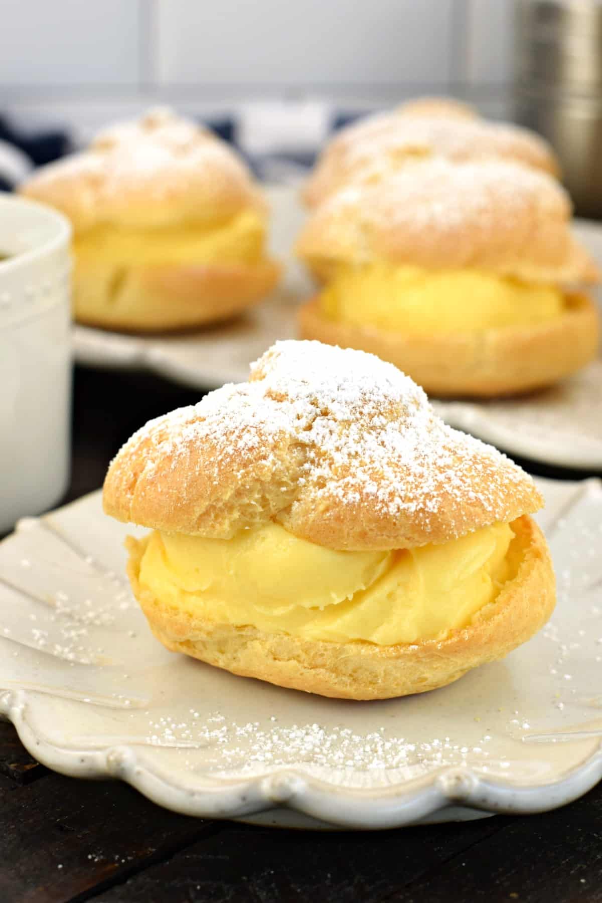 Cream puff on a white plate filled with custard and topped with powdered sugar.