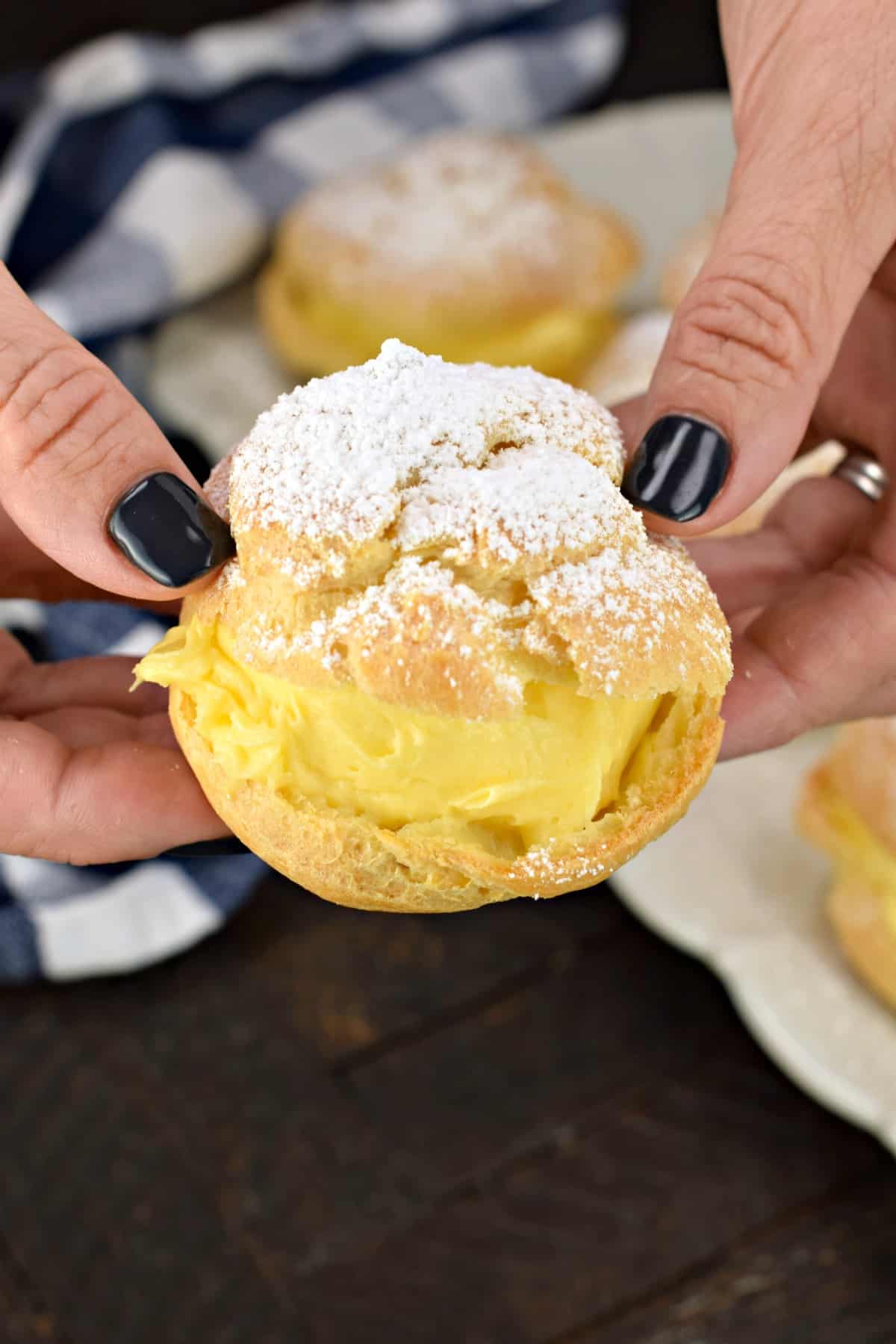 Two hands holding a powdered sugar cream puff.