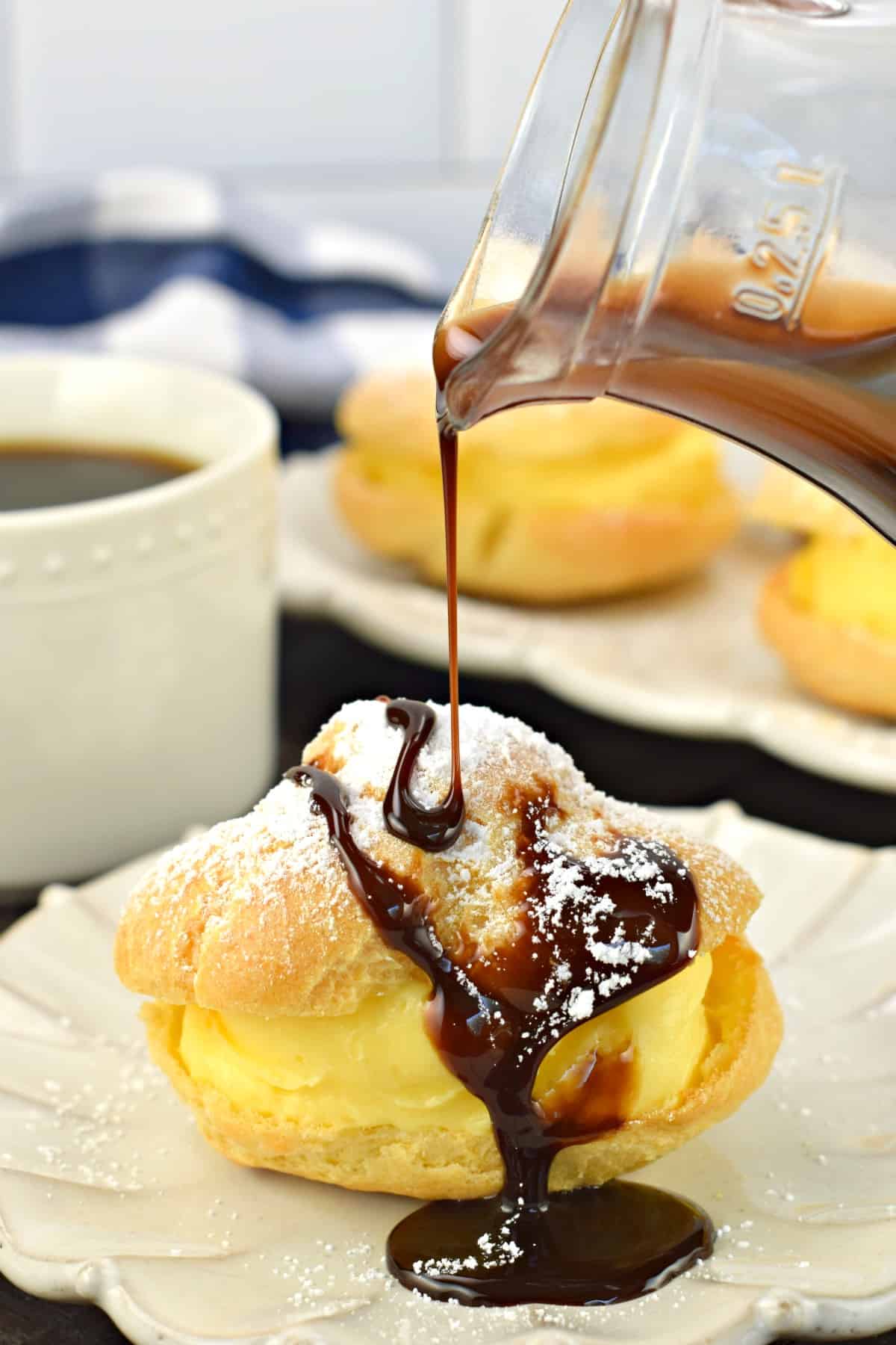 Chocolate syrup being poured over the top of a custard filled cream puff.