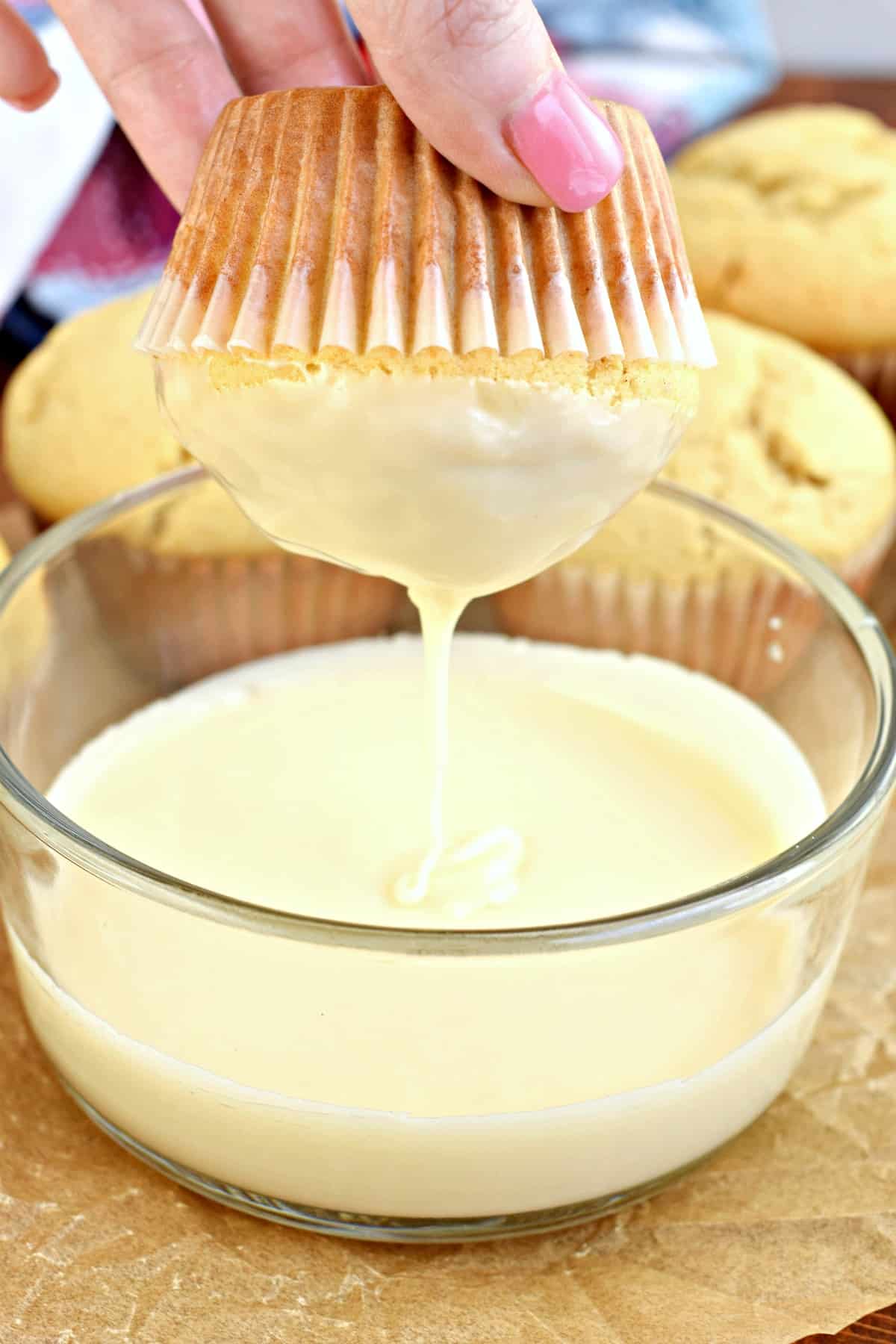 Donut muffin being dipped into a clear glass bowl of glaze.