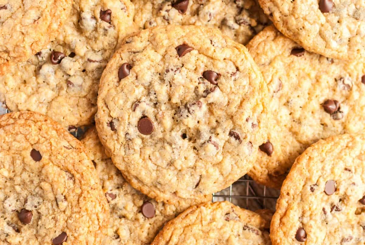 Piles of large chocolate chip cookies on wire rack.