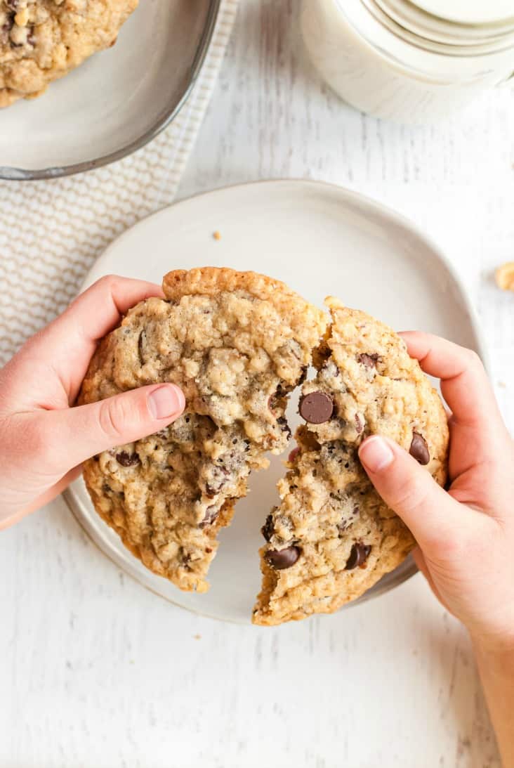 Small hands breaking a large chocolate chip cookie in half.